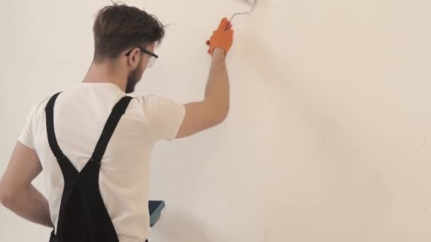 Maler in schwarzen Overalls bemalt weiße Wand mit Rolle — Stockvideo