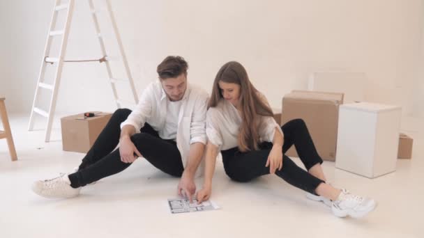 Pár se dívá na dům projekt sedí na podlaze s krabicemi — Stock video
