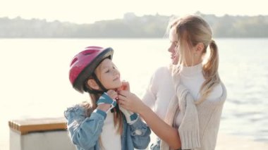 Genç anne kızına dışarıda kask takması için yardım ediyor.