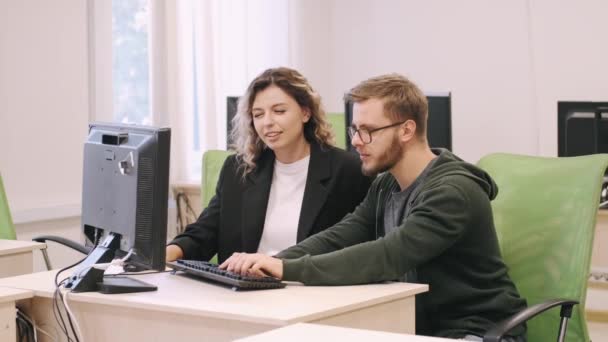 Un jeune homme et une jeune femme travaillent sur un ordinateur pendant qu'ils discutent d'un projet — Video