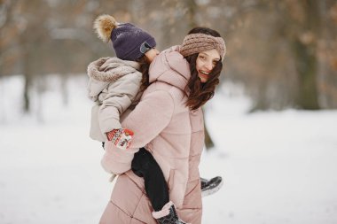 Anne ve çocuk kış kıyafetleriyle kış parkında oynuyorlar.