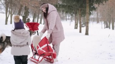 Anne ve kızı kışın kızakla parkta yürüyorlar.