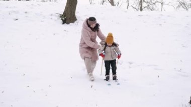Anne, kızına kış parkında kayak yapmayı öğretiyor.