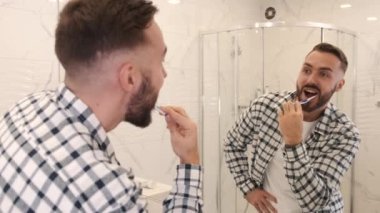 Diş fırçasıyla diş temizleyen genç adam ev banyosu yapıyor.
