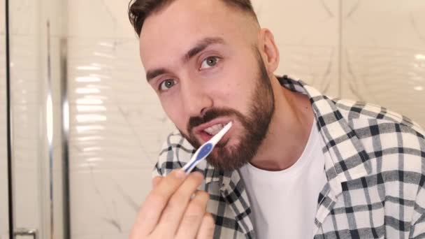 Ung man med tandborste rengöring tänder aat hem badrum — Stockvideo
