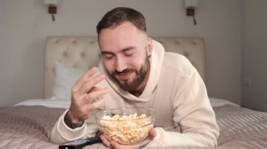 Genç adam yatakta uzanıyor ve evde televizyon izliyor.