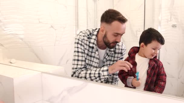 Homem pai ensina seu filho o menino no banheiro escovando dentes — Vídeo de Stock