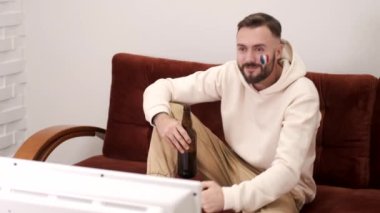 Genç adam yatakta uzanıyor ve evde spor televizyon izliyor.