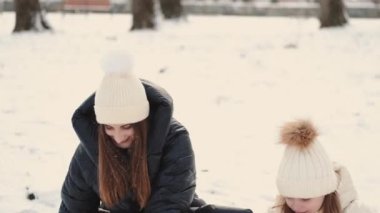 Anne ve kızı kış parkında karla oynuyorlar.