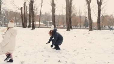 Anne ve kızı kış parkında karla oynuyorlar.