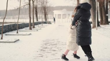 Anne ve kızı kış parkında el ele tutuşuyorlar.
