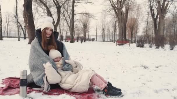 Мати і дочка мають пікнік на ковдрі в зимовому парку — стокове відео