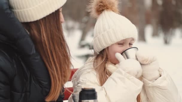 Joven madre con hija beber té caliente de un termo en el parque de invierno — Vídeo de stock