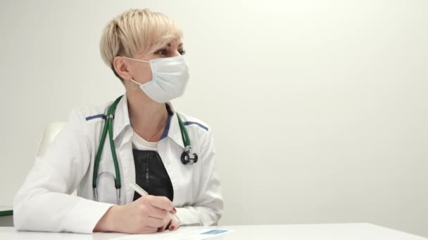 Жінка-лікар середнього віку в захисній масці розмовляє ро-пацієнт в клініці — стокове відео