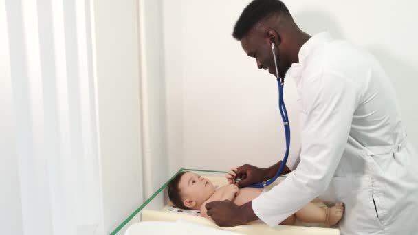 Pediatra médico negro masculino examinando al bebé en la clínica — Vídeo de stock