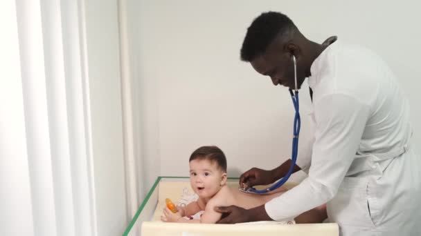 Pediatra médico negro masculino examinando al bebé en la clínica — Vídeos de Stock