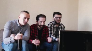 Arkadaşlar ekranın önünde oturup bira izlerler.