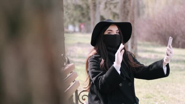 Молодая женщина в черном делает селфи в маске и перчатках — стоковое видео