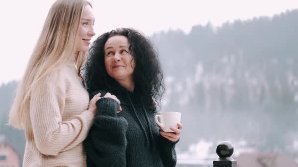 Mutter und schöne Tochter trinken Kaffee auf einem Balkon mit Berglandschaft — Stockvideo