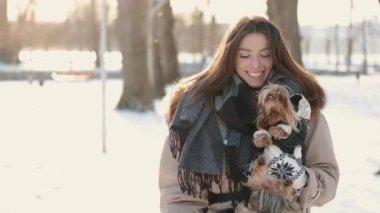Yorkshire Terrier köpeği olan mutlu genç bir kız kış parkında yürüyor.