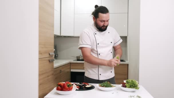 Chef en uniforme blanco preparando ensalada en cocina moderna — Vídeos de Stock
