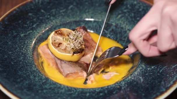 Женские руки режут рыбный стейк в супе в ресторане — стоковое видео