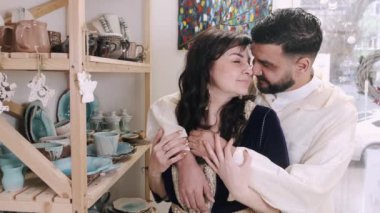 Orta yaşlı eşler çömlek atölyesinde birbirlerine sarılıyorlar.