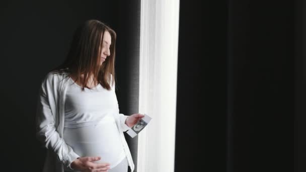 Zwangere vrouw staat bij het raam thuis — Stockvideo