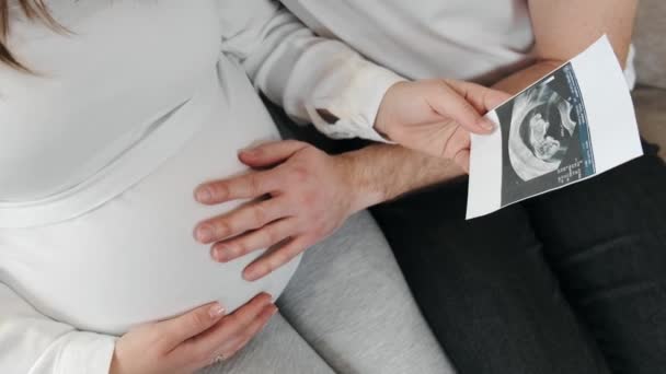 Echtgenoot knuffelen zijn zwangere vrouw zitten in gezellige kamer — Stockvideo