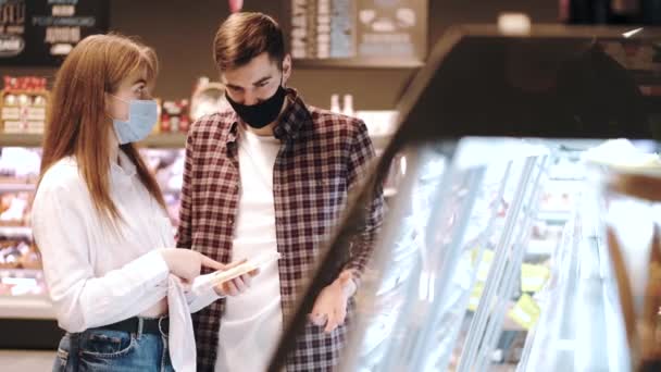 Couple dans des masques de protection faire du shopping au supermarché — Video