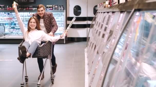 Homem feliz montando sua namorada no carrinho de compras — Vídeo de Stock