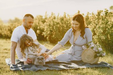 Küçük kızı olan bir aile güneşli bir arazide birlikte vakit geçiriyor.