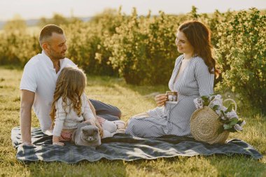 Küçük kızı olan bir aile güneşli bir arazide birlikte vakit geçiriyor.