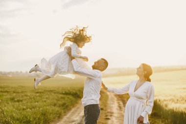 Küçük kızı olan bir aile güneşli bir arazide birlikte vakit geçiriyor.