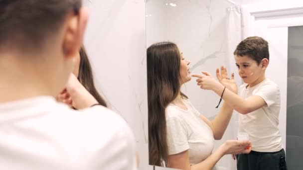 Zoon aanbrengen crème op moeders gezicht in de badkamer — Stockvideo