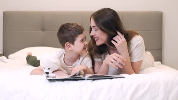 Glückliche Mutter und Sohn lesen gemeinsam Buch im Bett — Stockvideo
