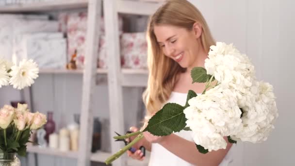 Молодая блондинка режет цветы в цветочном магазине — стоковое видео