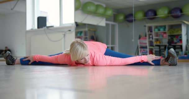 Frau in Sportbekleidung macht Dehnübungen am Boden im Fitnessstudio — Stockvideo