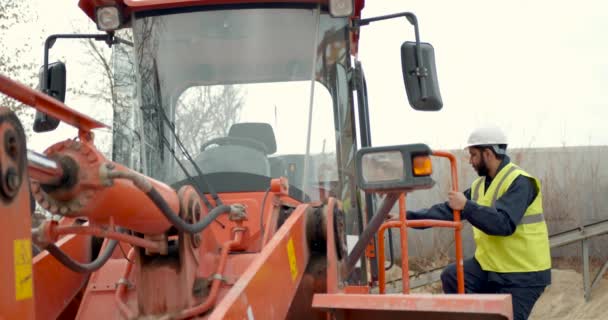 Man met helm komt trekker op bouwplaats binnen — Stockvideo