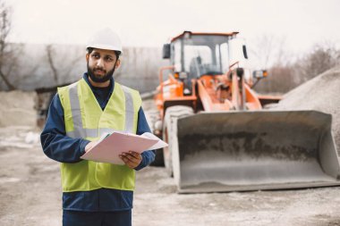 İnşaat mühendisi dışarıda kaskla çalışıyor.