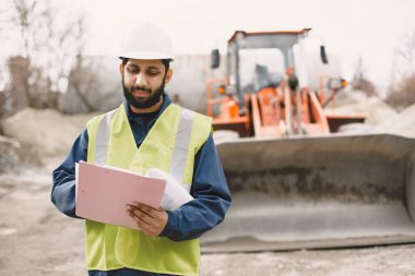 İnşaat mühendisi dışarıda kaskla çalışıyor.