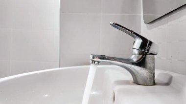 Banyodaki temiz beyaz seramik lavaboda açık bırakılan gümüş metal musluğu kapatan el görüntüsü. Su tasarrufu kavramı.