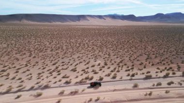 Las Vegas yakınlarındaki Mojave Çölü 'nde tek başına seyahat eden 4 tekerli siyah bir aracın görüntülerini izliyoruz.
