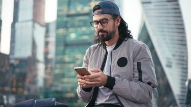 Elinde akıllı bir telefonla sokakta oturan yakışıklı genç adam.