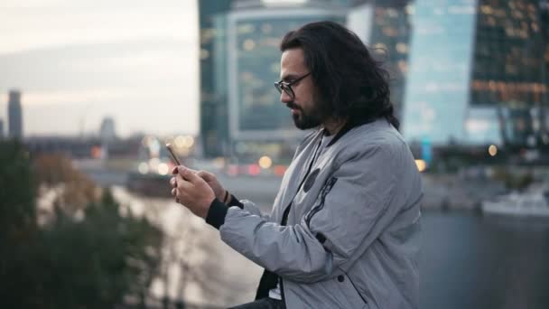 Beau jeune homme assis dans la rue avec un smartphone dans les mains — Video
