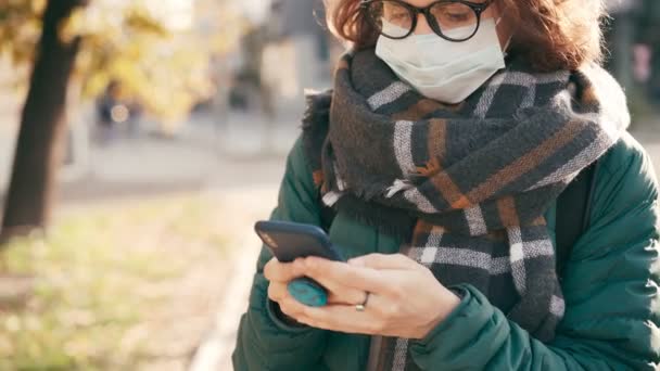 Una giovane donna con una maschera protettiva medica sta scrivendo un messaggio al telefono — Video Stock