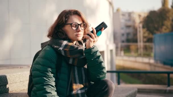 Una giovane donna in occhiali che registra un messaggio vocale sul suo telefono — Video Stock