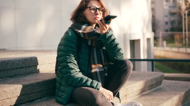 Una joven con gafas grabando un mensaje de voz en su teléfono — Vídeos de Stock