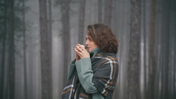 一位年轻女子裹着一条舒适的围巾，喝着热水瓶里的茶 — 图库视频影像
