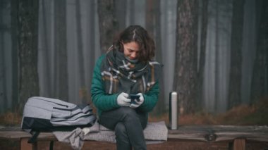 Sisli bir sonbahar ormanında akıllı telefonunu kullanan neşeli genç bir kadın..